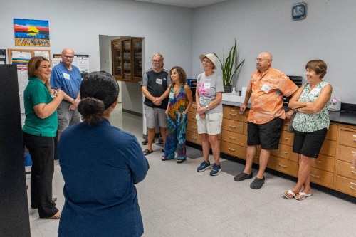 A group of CanalWatch volunteers stand in a lab, listening to a City staff member in a green shirt speak.
